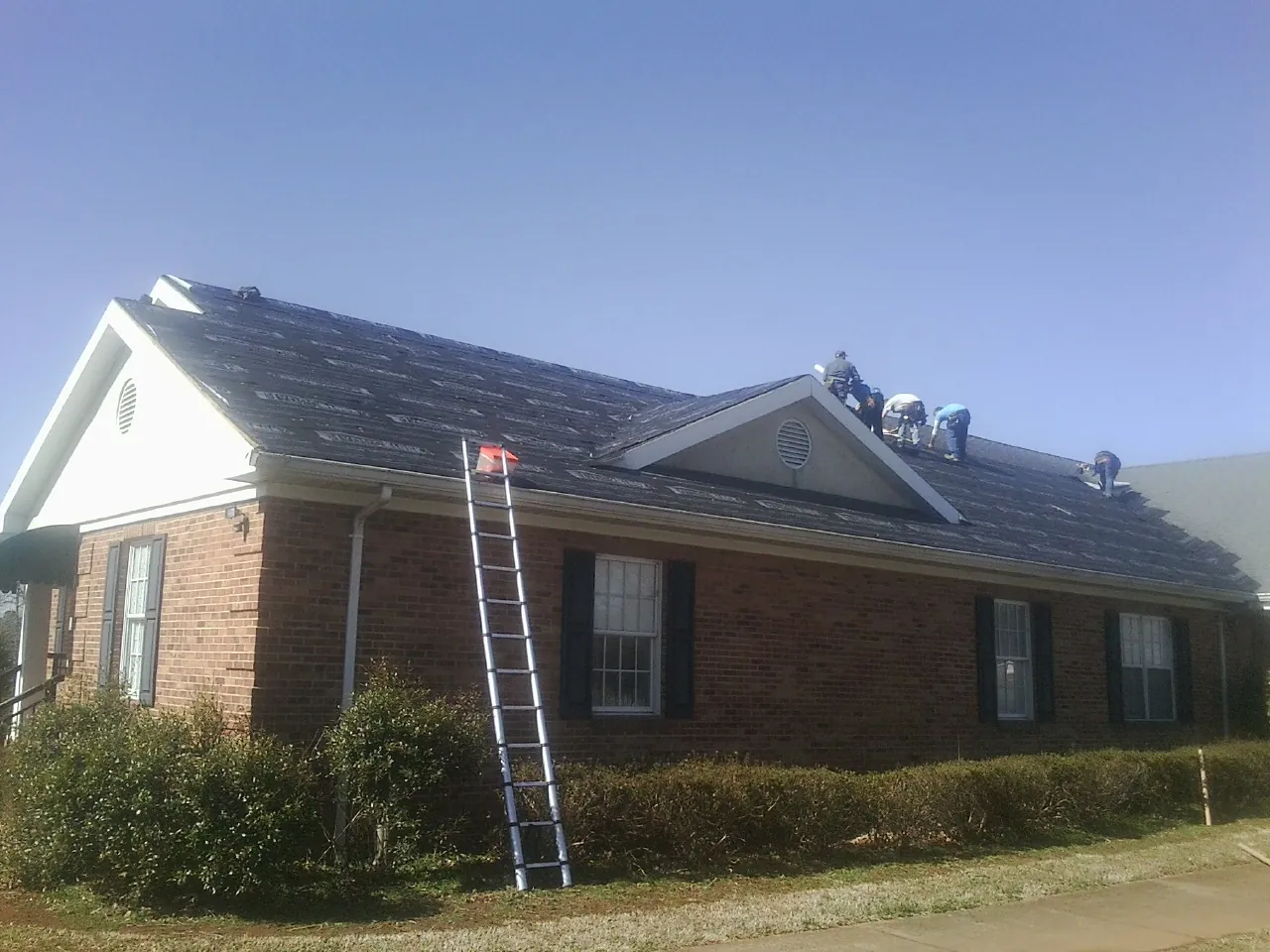 Crew tearing shingles off a brick ranch roof with a ladder set — Emergency Roof Repair work by our crew in Shady Side