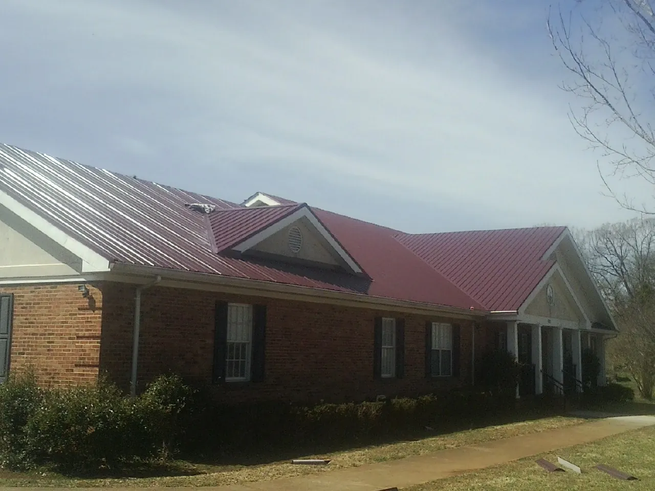 Red metal roof with gabled entries on a long brick building, from a Hail Damage Roof Repair job in Shady Side