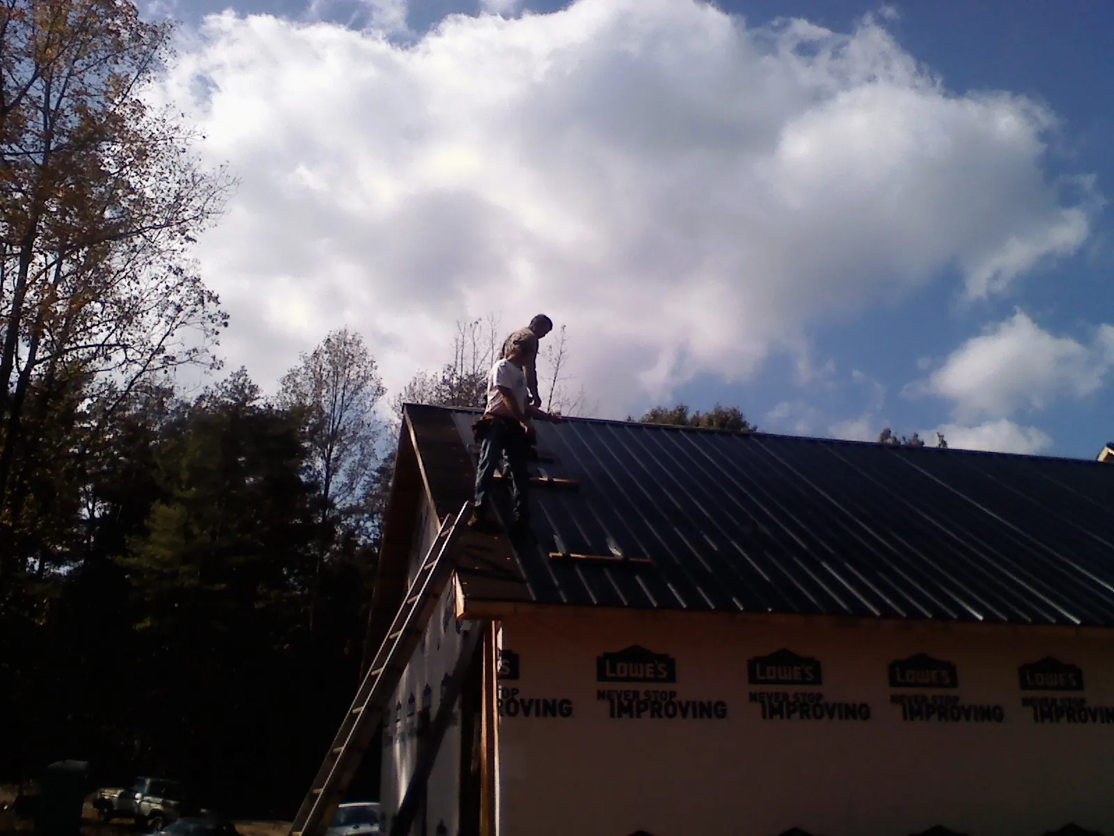 Roofer fastening dark metal panels high against a cloudy sky, from a Roof Inspection job in Shady Side