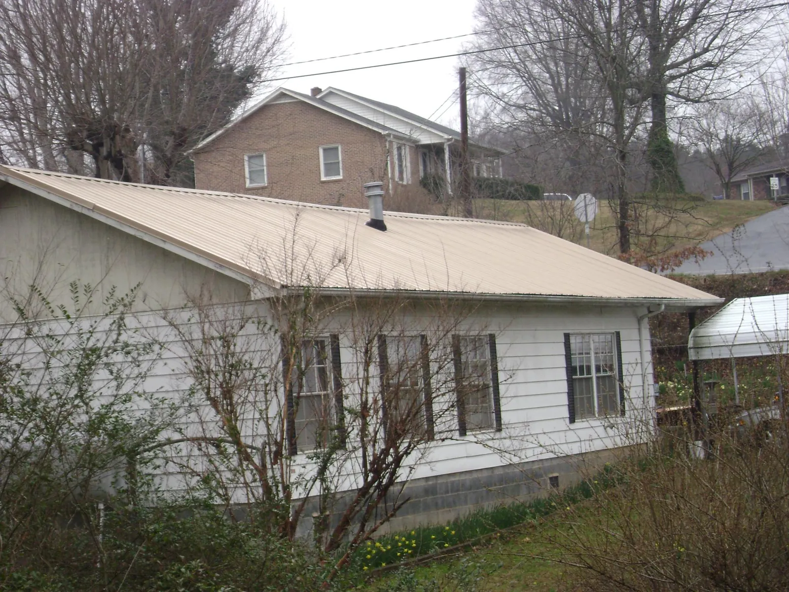 Tan metal roof on a white sided house set into a hillside — Commercial Roofing by Roofing Brothers in Shady Side